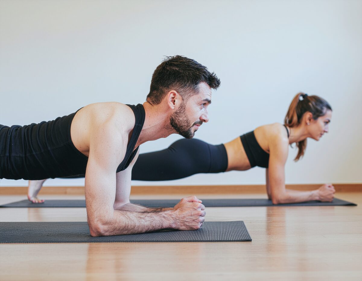 プランクをしている男女の画像。横からの視点。ジムでヨガマットを使用している。
