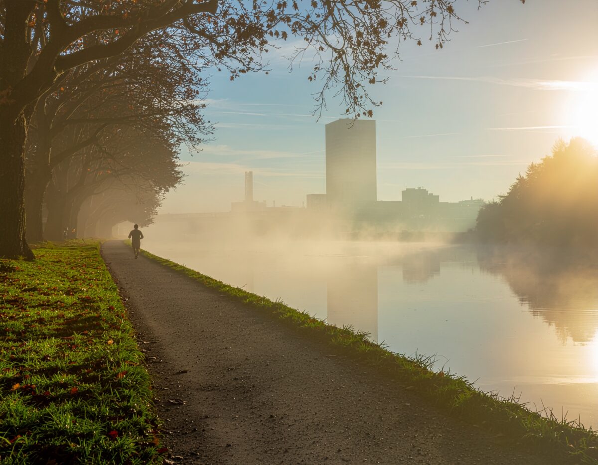朝のランニングをしているランナーと景色のイメージ、朝靄がかかり太陽の光が上がってきて水面に反射した朝ならではの美しさ。