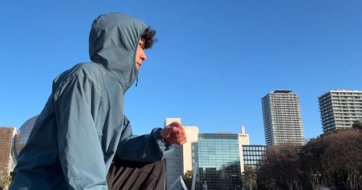 膝を立てて遠くを見ながらフードを被っている様子。どんな環境でも継続させる意志。